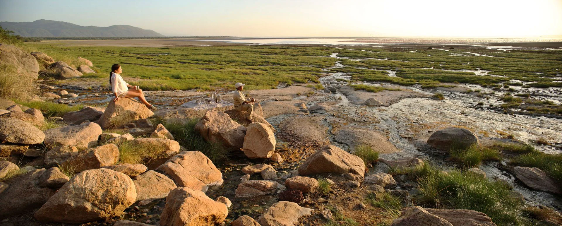 Travellers and their private guide overlooking an African wetland at sunset